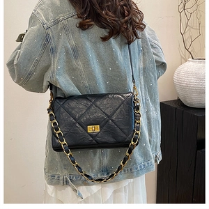 Detailed view of black quilted crossbody bag with gold chain strap worn by a model