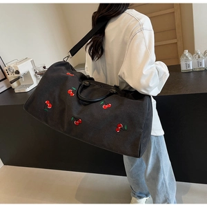 Detail of black canvas tote bag with red cherry embroidery and leather handle worn by model