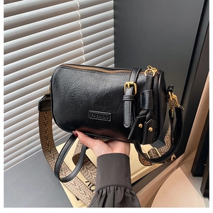 Détail du sac cylindrique noir avec texture litchi et bandoulière jacquard rétro