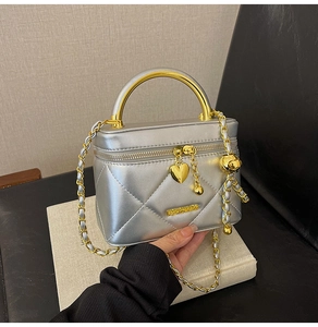 Detail of silver quilted handbag with golden handle, chain strap and heart charm decoration