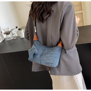 Blue denim crossbody pillow bag with brown leather trim and side bow detail on a model