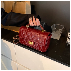 Close-up of wine red quilted patent leather handbag with gold metal clasp and chain