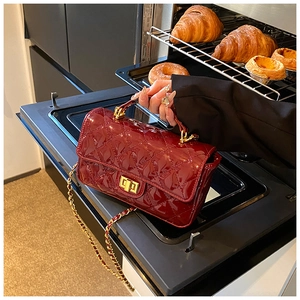 Detail of burgundy quilted patent leather handbag with gold metal lock and chain strap
