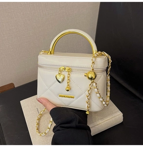 Detail of quilted mini handbag with gold metal handle and heart pendant on books
