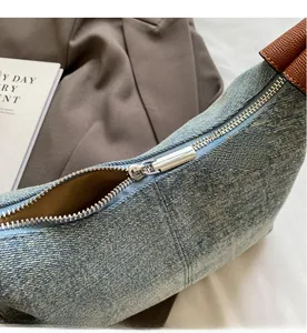 Detail of silver metal zipper on blue denim handbag with brown leather trim finish