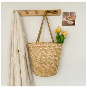 Close-up of handwoven straw bucket bag with rope strap and tulip flowers on a wall hook