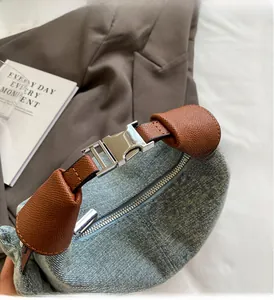 Detail of denim handbag with brown leather handle and silver buckle on a textured blazer
