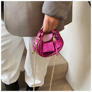 Detail of fuchsia patent leather mini hobo bag with gold chain strap held by a model