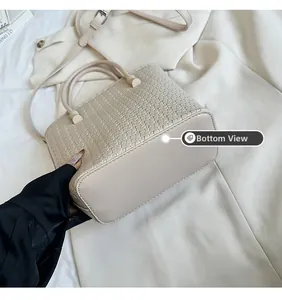 Dettaglio della borsa a secchiello intrecciata beige che mostra la base solida in PU