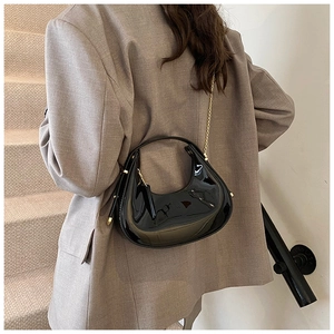 Detail of a black patent leather crescent bag with a gold chain on a suit-clad model