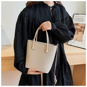 Dettaglio borsa a secchiello intrecciata beige chiaro con doppi manici e tracolla