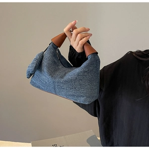 Detail of blue denim pillow bag featuring large fabric bow and brown leather handles