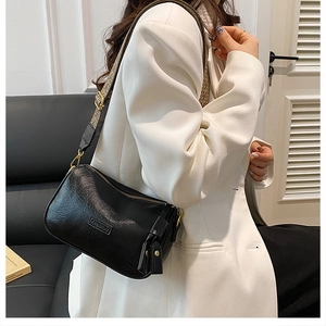 Détail d'un sac bandoulière noir avec sangle large à motifs sur un mannequin en blazer