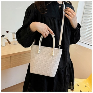 Dettaglio di una borsa a secchiello intrecciata bianca con manici e tracolla regolabile