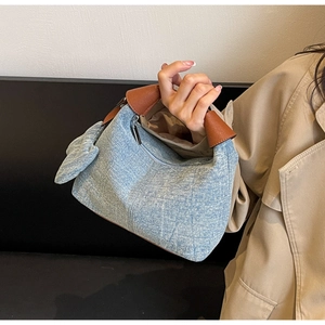 Detail of blue denim pillow bag with brown leather handle and stylish denim bow accent