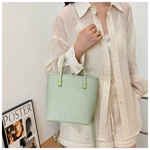 Dettaglio della borsa a secchiello verde chiaro intrecciata con texture esterna e manici