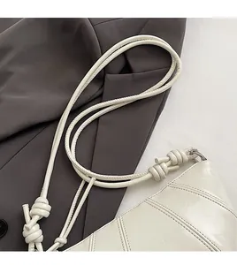 Detail of white glossy dumpling bag showing elegant knotted shoulder strap design