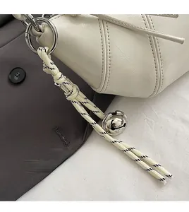 Detail of white leather shoulder bag featuring woven rope and a silver bell charm accent