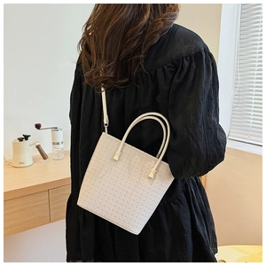 Dettaglio della borsa tote intrecciata bianco crema indossata in un interno minimalista