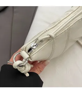 Detailed close-up of smooth silver zipper and quilted texture on cream crossbody bag