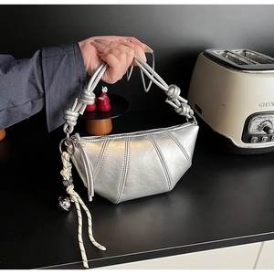 Detail of silver metallic textured dumpling bag featuring knotted handle and creative charms