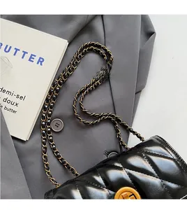 Gros plan d'un sac matelassé noir avec chaîne dorée posé sur un blazer gris