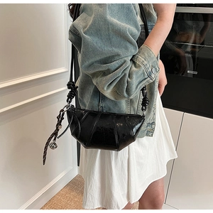 Detail of black croissant bag with knotted strap and metal charm on a model