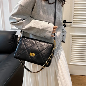 Chic black quilted shoulder bag with gold chain strap worn by a model in a modern home