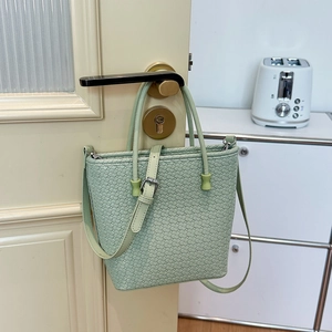 Dettaglio borsa a mano verde chiaro con trama intrecciata appesa a una maniglia con tracolla