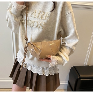 Detail of khaki patent leather croissant crossbody bag with pleated finish and knotted strap