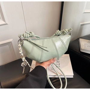 Detail of light green pleated croissant bag with glossy texture and knotted strap design