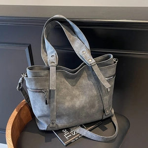 Dunkelgraue Shopper-Tasche mit Nieten und verstellbarem Riemen auf einem Vintage-Stuhl