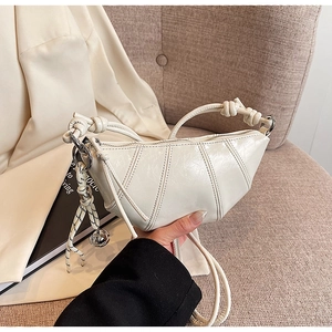 Detail of cream crossbody bag with glossy wrinkled texture and silver bell charm