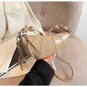 Detail of light beige glossy crescent bag with knotted handle and metal ball charm