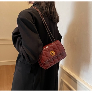Détail du sac matelassé bordeaux avec fermoir doré sur une veste de blazer noire