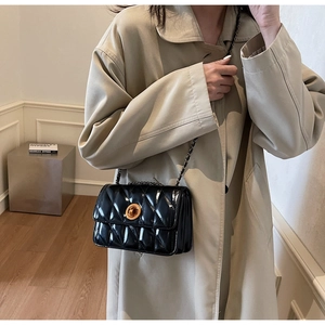 Détail d'un sac à bandoulière matelassé noir avec fermoir doré porté par un mannequin