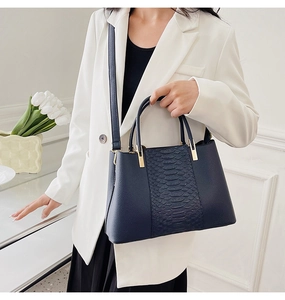Detail of navy blue croc-embossed tote bag held by a model in a white blazer
