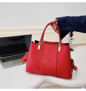 Detail of red tote bag featuring crocodile pattern texture and golden metal hardware