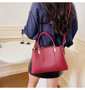 Detail view of red crocodile-pattern tote bag with golden hardware and detachable strap