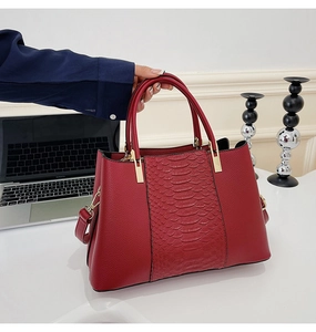 Close-up of red tote bag with crocodile pattern and golden metal buckles details