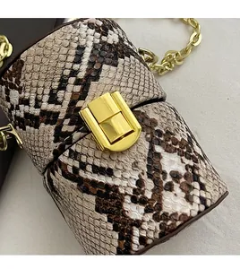 Gros plan d'un mini sac cylindre imprimé serpent avec chaîne dorée et fermoir métal