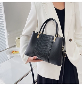 Detail of crocodile embossed leather and gold hardware on black tote bag