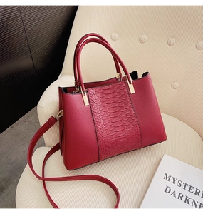 Detail of burgundy crocodile pattern handbag with gold hardware on a textured sofa