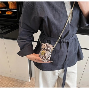 Mini sac cylindrique motif serpent avec chaîne dorée et fermoir dans un décor de cuisine