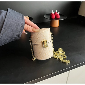 Détail du mini sac cylindrique crème avec texture autruche et bandoulière chaîne dorée
