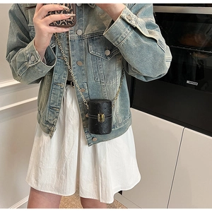 Mini sac cylindrique noir texture autruche avec chaîne dorée porté sur robe blanche