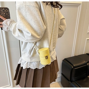 Détail d'un mini sac seau jaune à texture autruche avec bandoulière chaîne dorée sur modèle
