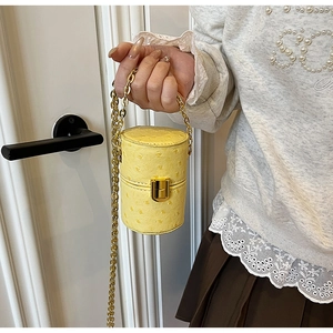 Détail du mini sac seau jaune à motif autruche avec chaîne dorée tenu à la main
