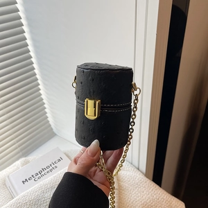 Mini sac cylindrique noir avec texture autruche et chaîne dorée dans un cadre épuré