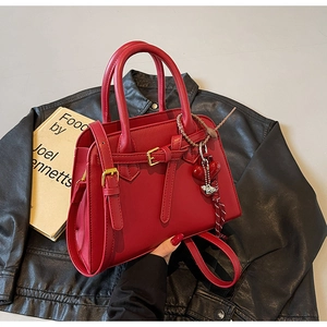 Detail of red leather tote bag with heart charm and striped lanyard on black background